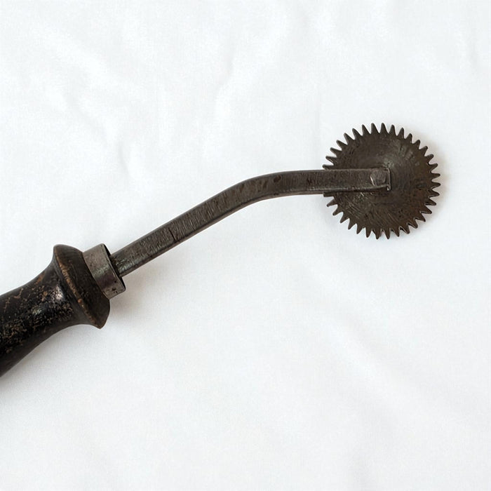 Vintage metal tool with a curved blade and circular wheel on a white background