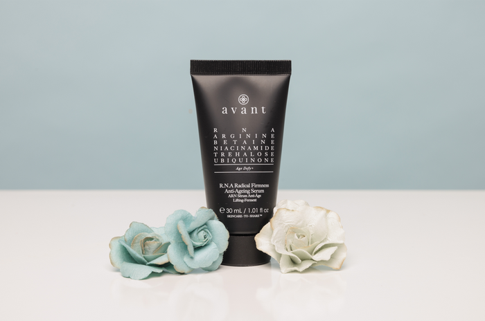 Black tube of Avant skincare product on a white surface with decorative flowers against a light blue background