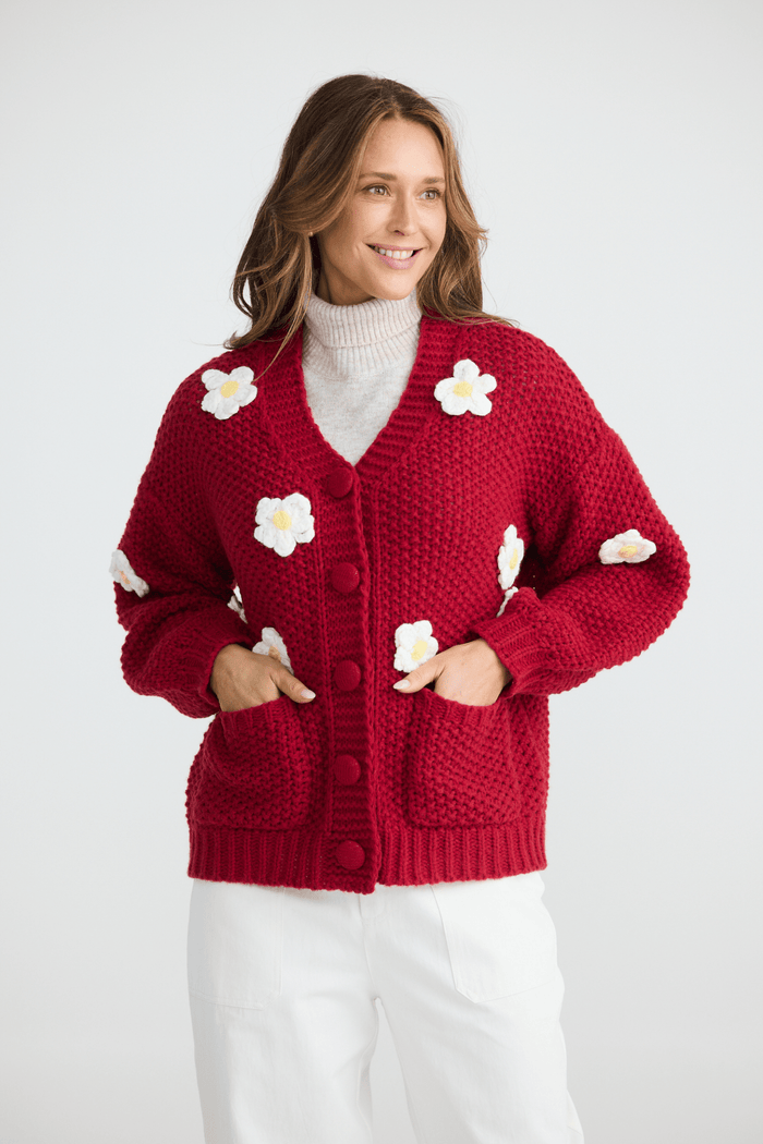 Woman wearing a red cardigan with white flower patterns on a white background