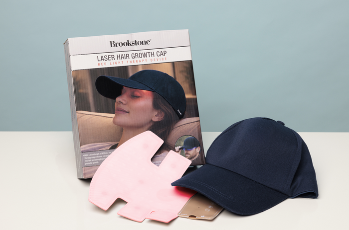 Navy laser hair growth cap with pink device and Brookstone packaging on a light surface.