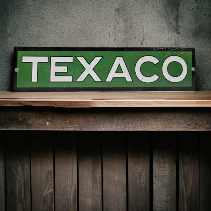 Vintage Texaco sign on a wooden shelf against a concrete wall.