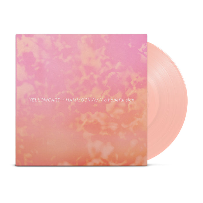 A creamsicle colored vinyl peeks out of a jacket with a picture of tree branches with a strong pink-orange tint applied. The words "Yellowcard + Hammock" and "A Hopeful Sign" are in the center of the image.