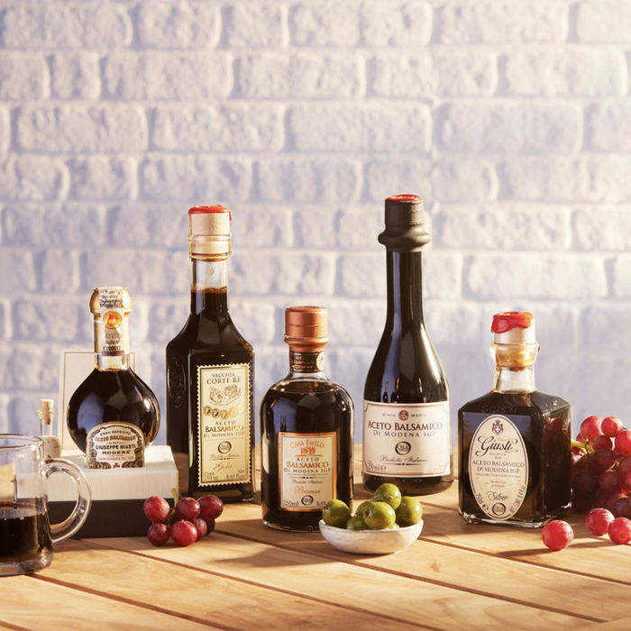 five dark bottle of balsamic vinegar on a wooden table with grapes scattered around.