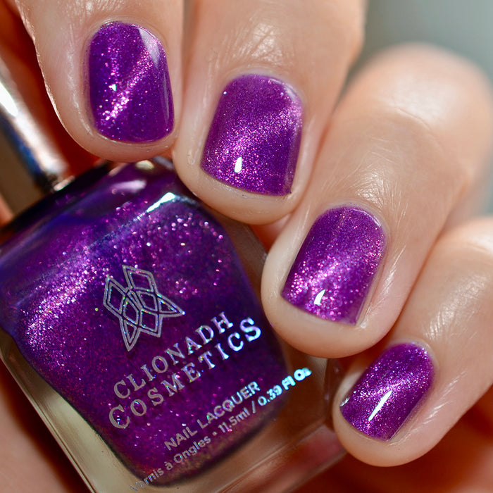 Close-up of nails painted with Anthocyanin Nail Lacquer on fair skin tone. Hand is holding polish bottle.