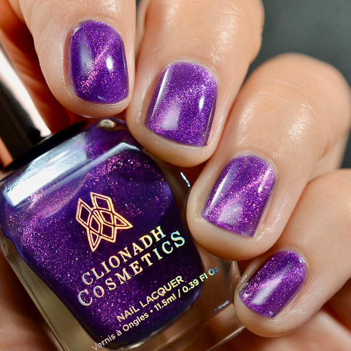 Close-up of nails painted with Anthocyanin Nail Lacquer on fair skin tone. Hand is holding polish bottle.