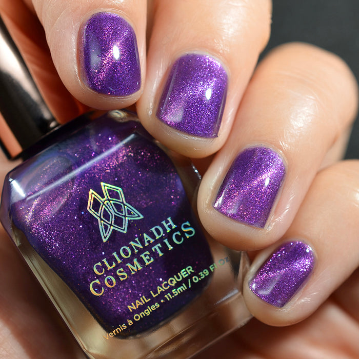 Close-up of nails painted with Anthocyanin Nail Lacquer on fair skin tone. Hand is holding polish bottle.