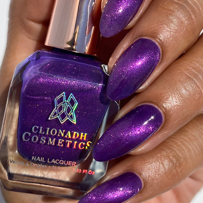 Close-up of nails painted with Anthocyanin Nail Lacquer on medium skin tone. Hand is holding polish bottle.