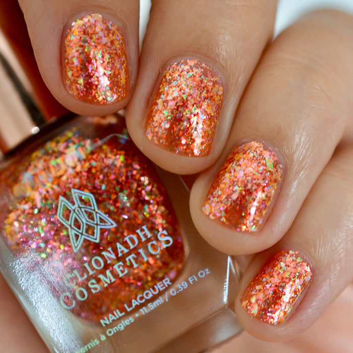 Close-up of nails painted with Autumn Acres Nail Lacquer on fair skin tone. Hand is holding polish bottle.