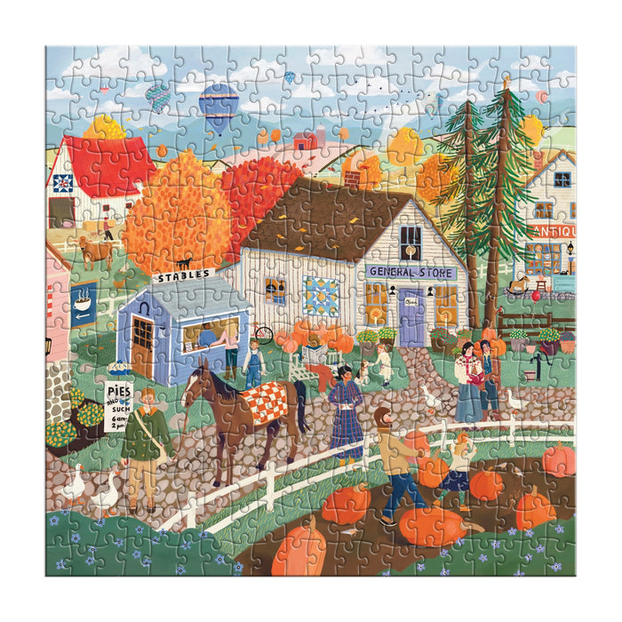 The Autumn Square 300 Piece Puzzle by Elisabeth Dorrian features a vibrant fall village with people, pumpkins, a horse at stables, a general store, an antiques shop, and colorful autumn trees.