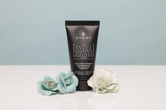 Black tube of Avant skincare product on a white surface with decorative flowers against a light blue background