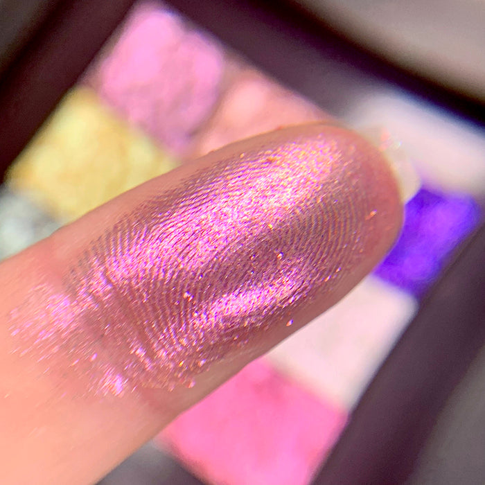 Close-up finger swatch of Baroness Eyeshadow on fair skin tone. Blurred palette in the background.