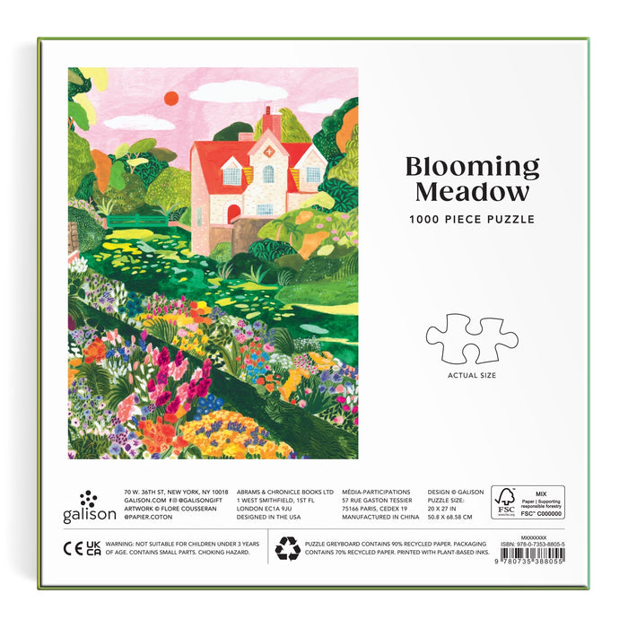 The Flore Cousseran Blooming Meadow 1000 Piece Puzzle features a house with a red roof amid vibrant flowers and greenery under a blue sky; it includes a puzzle piece graphic showing the actual size.
