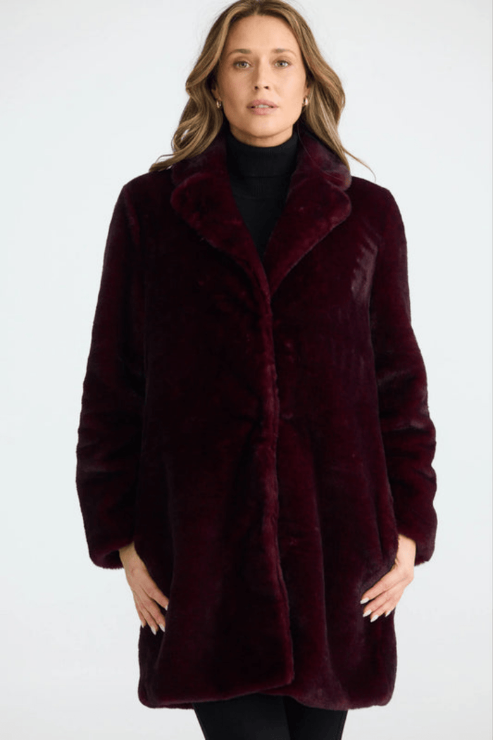 Woman wearing a burgundy faux fur coat on a white background