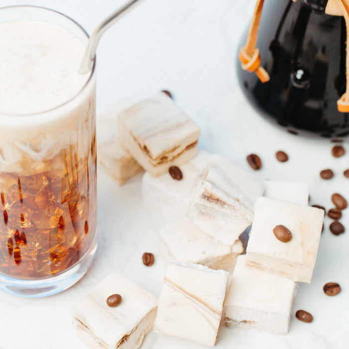 An overhead shot of a glass of iced coffee and caffeinated marshmallows against a marble background