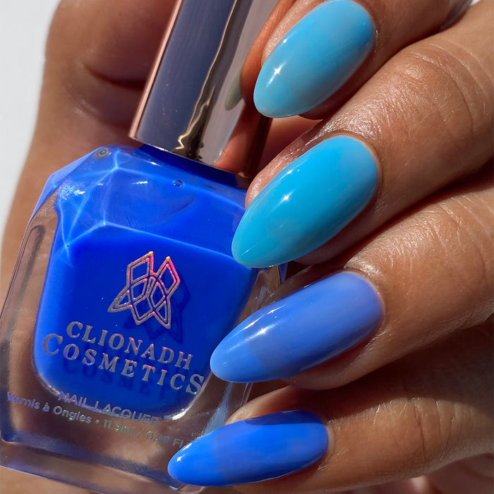 Close-up of nails painted with Cumulus Nail Lacquer on medium skin tone. Hand is holding polish bottle.