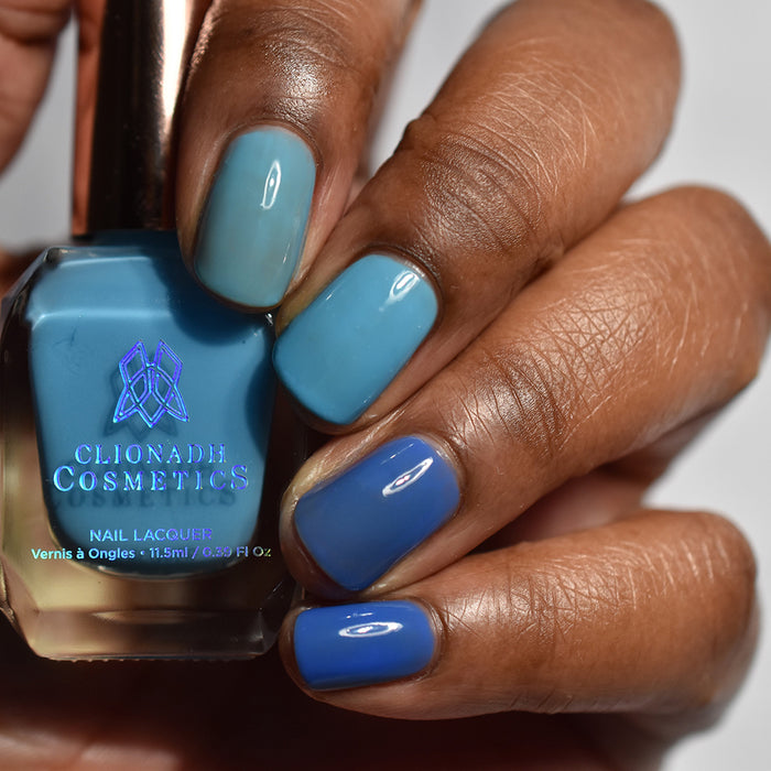 Close-up of nails painted with Cumulus Nail Lacquer on deep skin tone. Hand is holding polish bottle.