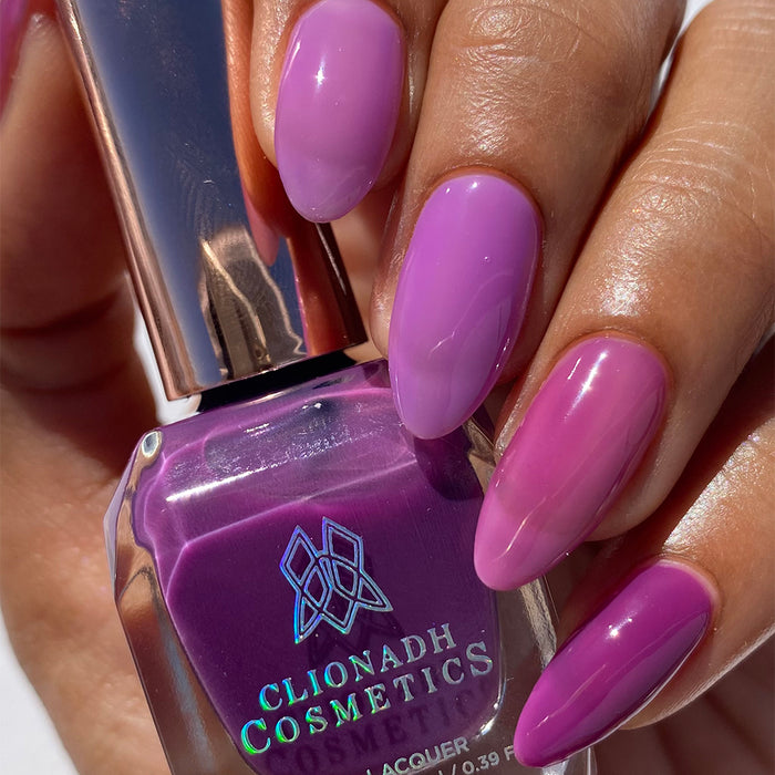 Close-up of nails painted with Euphoric Nail Lacquer on medium skin tone. Hand is holding polish bottle.