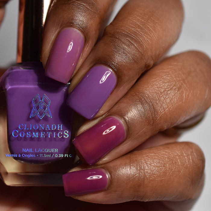 Close-up of nails painted with Euphoric Nail Lacquer on deep skin tone. Hand is holding polish bottle.