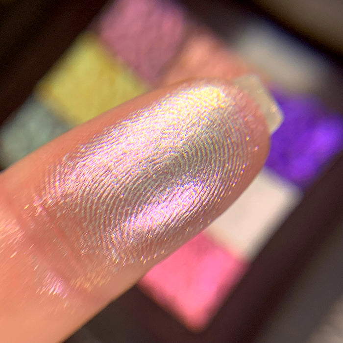Close-up finger swatch of the eyeshadow Facet on fair skin tone. Blurred palette in the background.