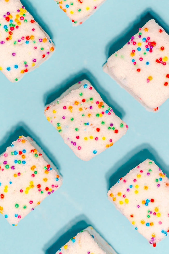 An overhead grid photo of the Funfetti homemade marshmallows against a blue background. All of the marshmallows are covered in natural dye sprinkles.
