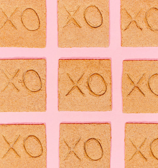 A grid of nine gluten-free graham crackers with 'XO' stamped onto them arranged on a pink background.