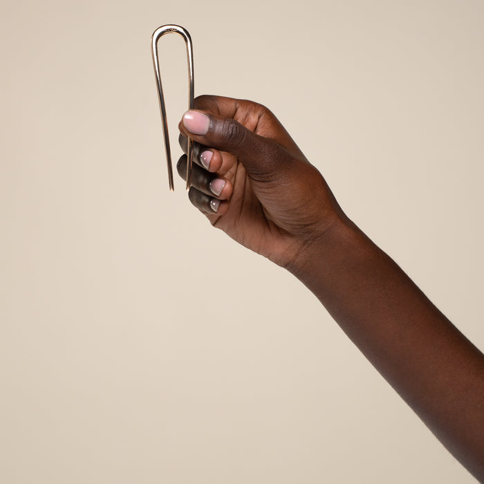 Hand holding kitsch gold mini metal clip against a beige background