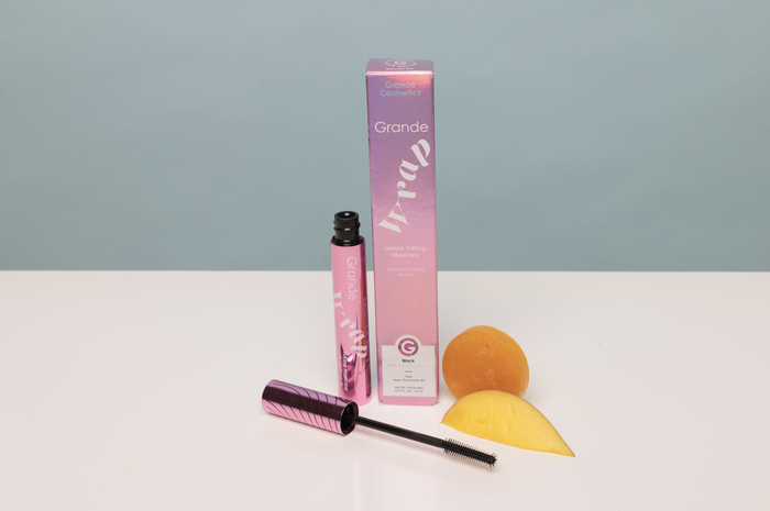 Cosmetic products including a pink tube, brush, and packaging on a white surface with a light blue background.