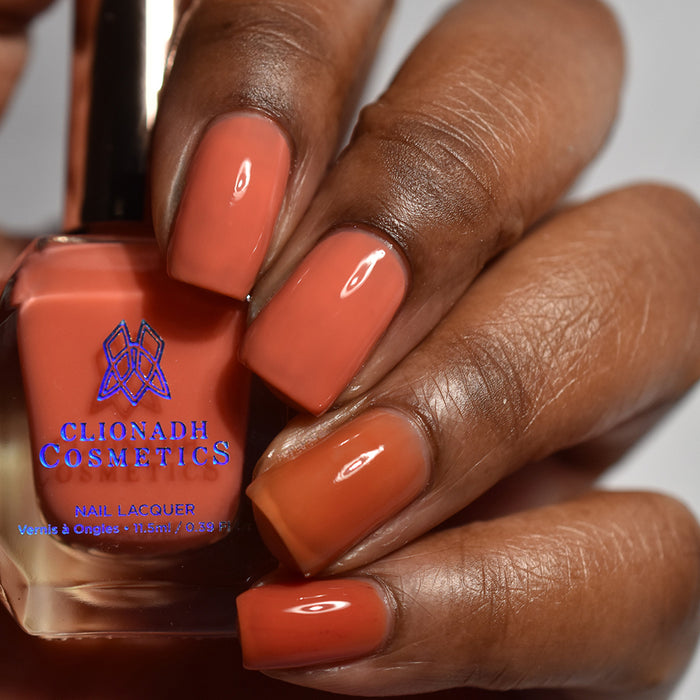 Close-up of nails painted with Horizon Nail Lacquer on deep skin tone. Hand is holding polish bottle.