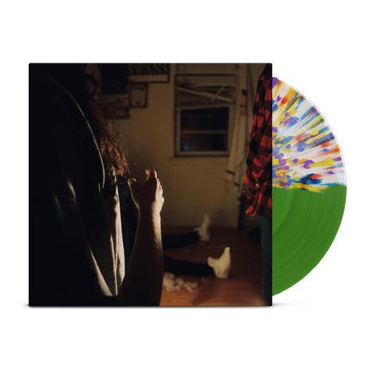 A half green and half clear with rainbow splatter vinyl peeks out of a jacket with the image of three Kaonashi members in front of a window in a house with broken down blinds. The closest member is only showing his arms and hair, with the second only showing his red flannel, and the third sitting down with white shoes.