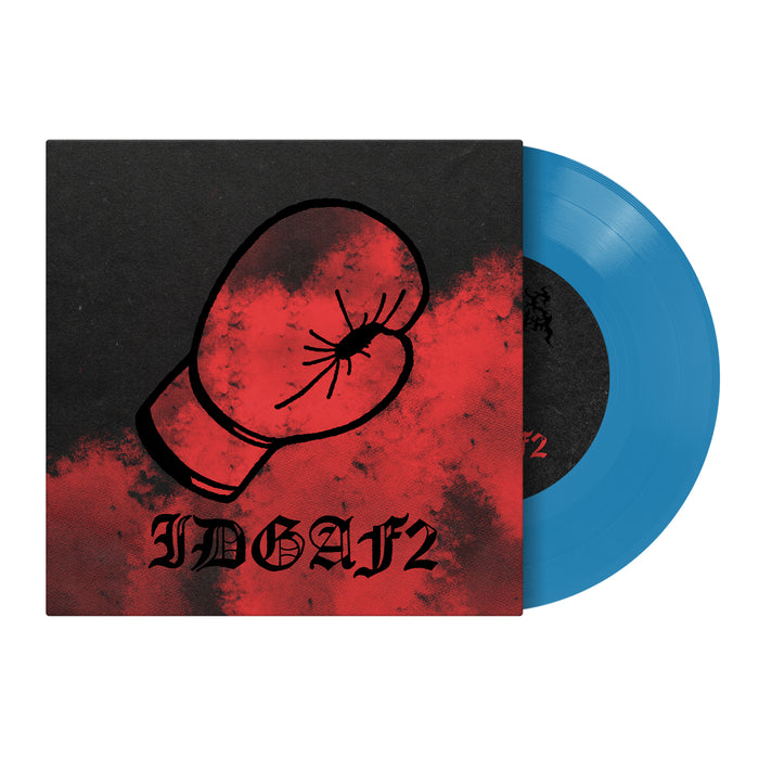 A blue vinyl record by Dwellings partially slides from a black and red album cover with a red boxing glove and bold IDGAFII text, hinting at the tracklist with songs like "Just A Man.