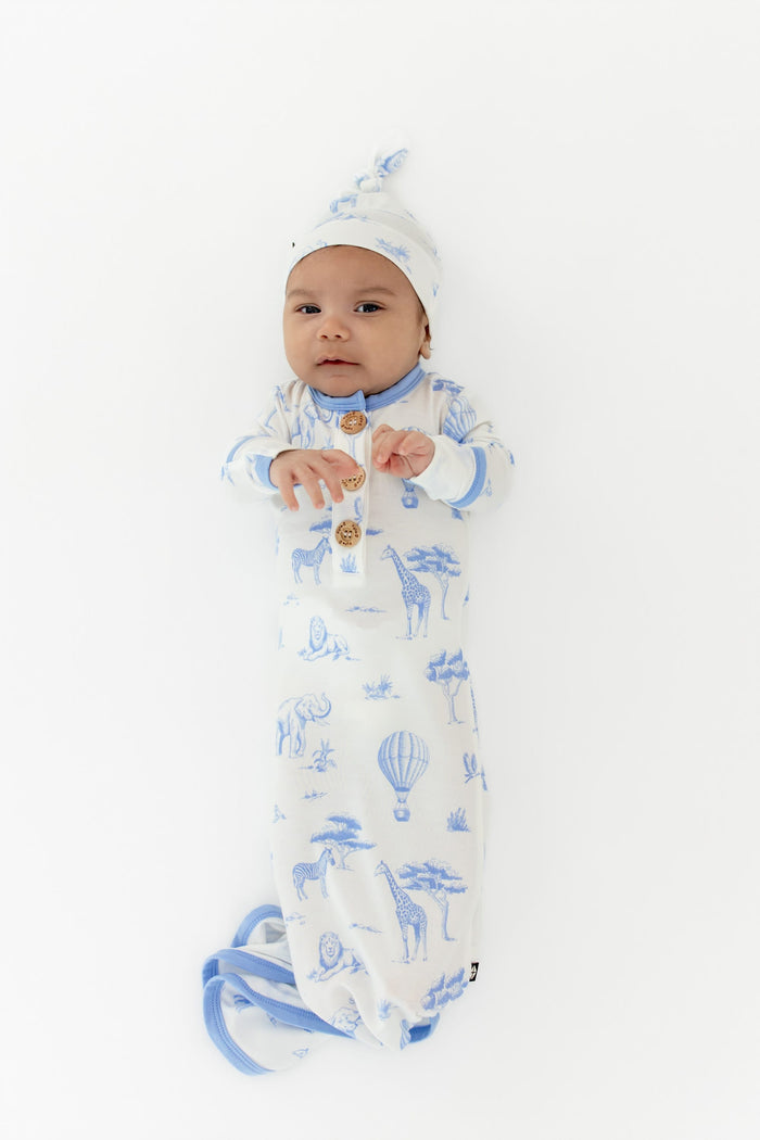 Newborn laying on a white surface wearing the Knotted Gown with Hat Set in Toile Safari