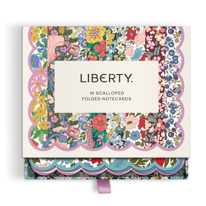 The Liberty Premium Notecard Set by Liberty London features 16 scalloped, folded notecards with vibrant floral designs. The box, labeled LIBERTY, has a purple ribbon tab and is slightly open to display the colorful cards inside.