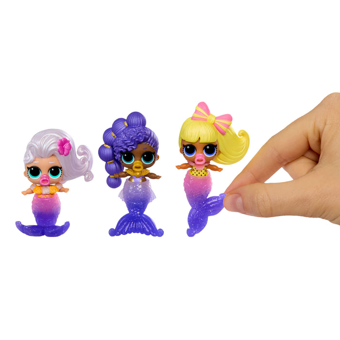 Three small mermaid figurines with colorful hair and tails on a white background, with a hand reaching towards them.