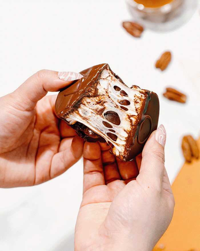 A gif showing a marshmallow turtle being pulled apart so you can see all of the ooey gooey laters of caramel and marshmallow beneath the chocolate shell