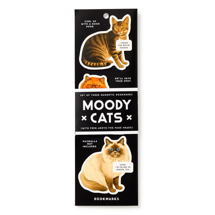 The Brass Monkey Moody Cats Magnetic Bookmark Set includes three cat-shaped bookmarks with illustrated cats and speech bubbles on a black background. The packaging says Moody Cats (with peek-above-the-page heads) Magnetic Bookmarks.
