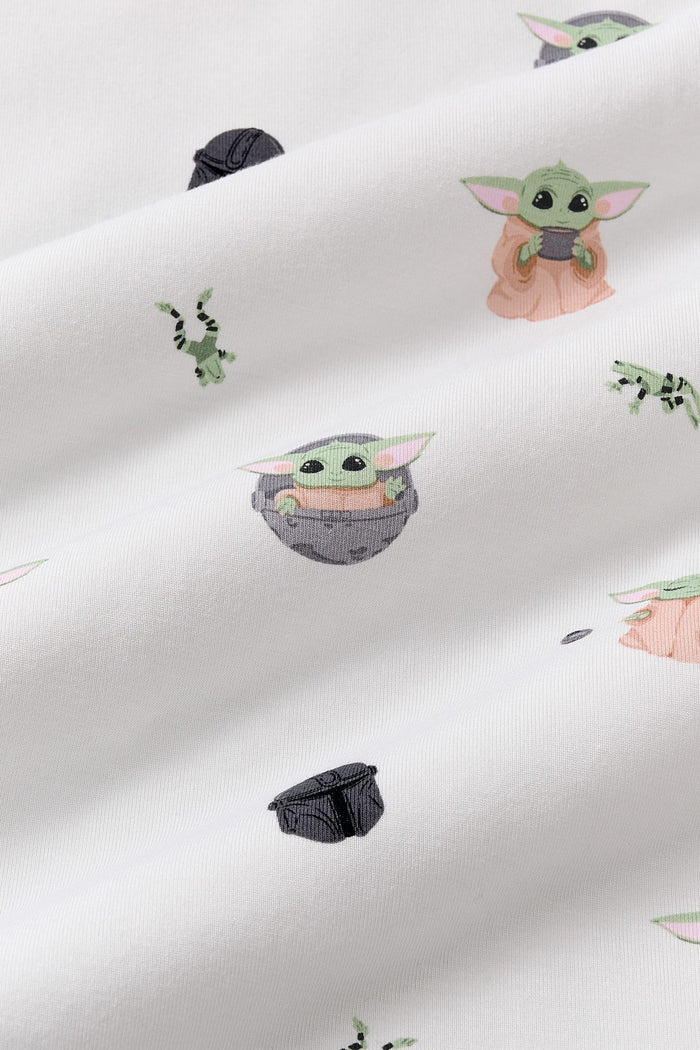 Close up of the bamboo fabric: A repeating, all-over print featuring Grogu in a hover pram; a dark grey Mandalorian helmet; Grogu holding a grey cup; Grogu with his eyes closed, telekinetically manipulating a small silver ball; and leaping green Arges Frogs with black stripes, over a white background.