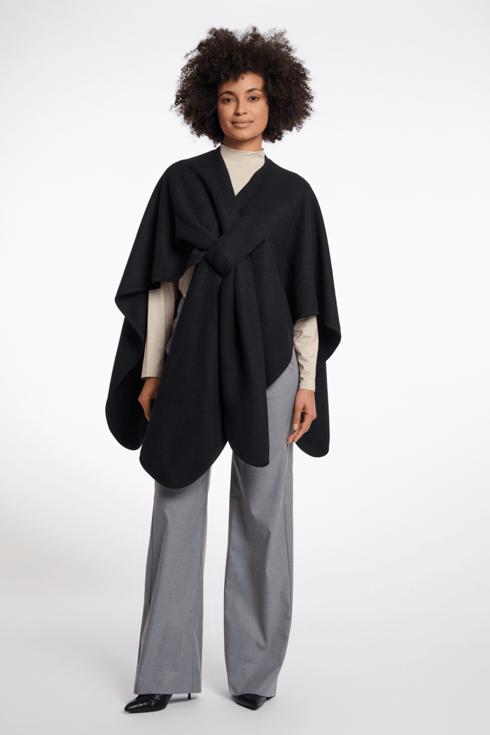 Woman wearing a black poncho over a beige top and gray pants on a white background