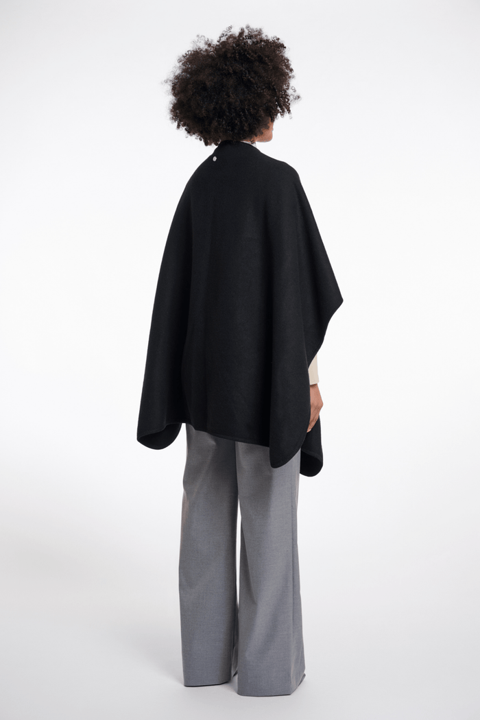 Person wearing a black cape and gray pants on a white background