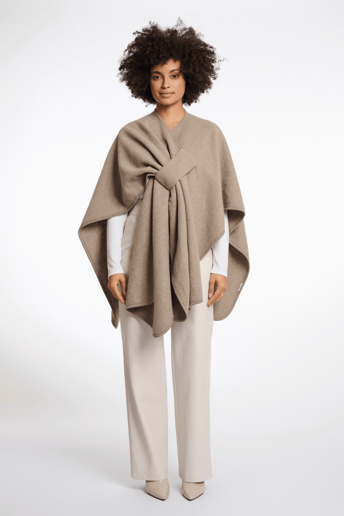 Woman wearing a beige poncho over a white outfit on a white background