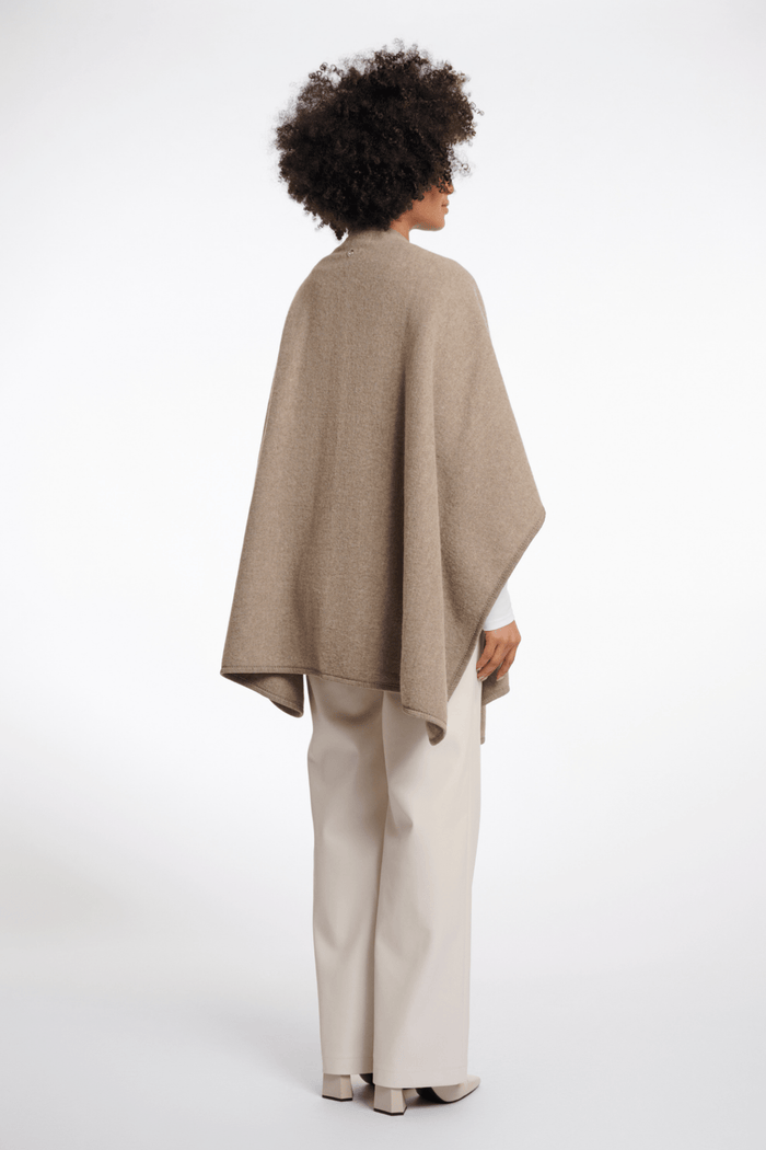 Person wearing a beige poncho and pants on a white background