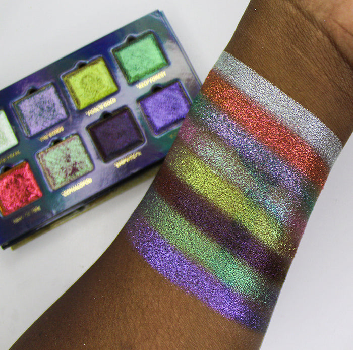 Arm swatches on deep skin tone of all eight eyeshadows included in the Deep Sea Treasures Palette, with palette in background.