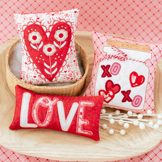 Three decorative pillows with heart designs on a pink textured background