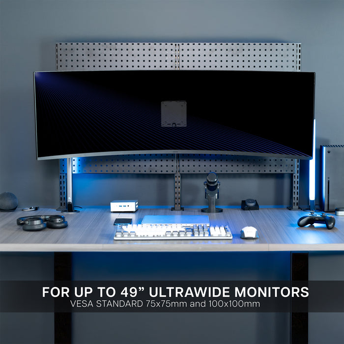Desk setup with a large ultrawide monitor mounted to a pegboard, keyboard, and mouse in a dark room.