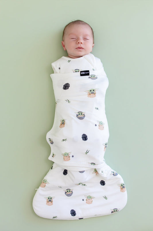 Sleeping newborn swaddled in the Sleep Bag Swaddler in Grogu™ 1.0 on a light green background