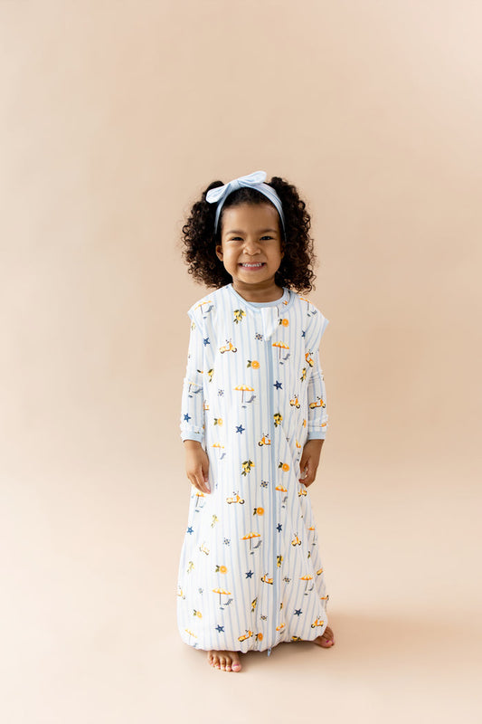 Smiling girl wearing the Sleep Bag Walker in Amalfi Coast 1.0 with light blue bow