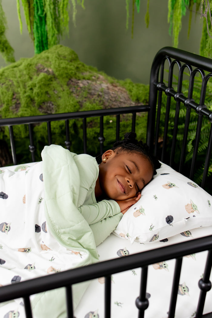 Young girl sleeping in bed laying her head on the Toddler Pillowcase in Grogu™ with the matching toddler blanket on top of her