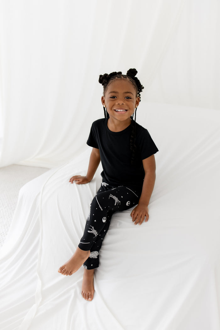 Young girl sitting on a white blanket wearing the Toddler Leggings in STAR WARS™ with a basic tee in black