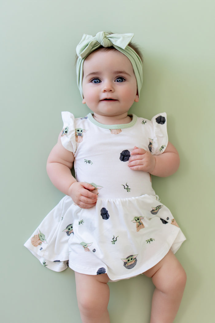 Young girl infant wearing the Twirl Bodysuit Dress in Grogu™ with a light green bow