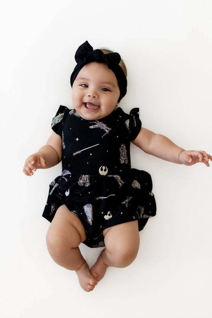 Smiling infant laying on a white surface wearing the Twirl Bodysuit Dress in STAR WARS™