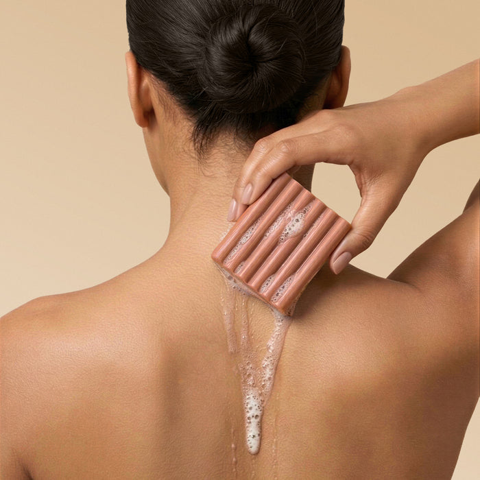 Woman lathering Kitsch Amber Shores Body Wash Bar on her back with sudsy foam on a beige background